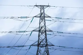 A power line pole seen obliquely from below against a sky with a white cloud cover of varying thickness in the background.