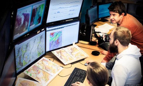 Meteorologer diskuterar framför skärmar i SMHIs prognoscentral, foto.