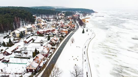 Vinterlandskap med ett samhälle och en kustnära väg med utsatt läge intill den is- och snöbelagda Östersjön.