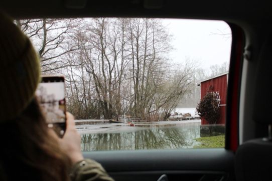 Olivias bakhuvud syns när hon fotograferar en översvämmad trädgård med sin mobilkamera.