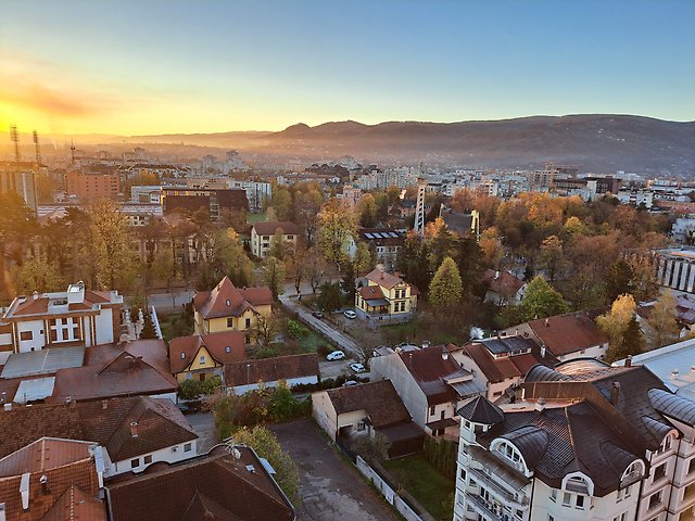 Vy över Banja Luka i Bosnien och Hercegovina en novembermorgon. Bostadshus, träd och stadsmiljö syns i förgrunden medan ett dis ligger över staden och de omgivande kullarna i bakgrunden.