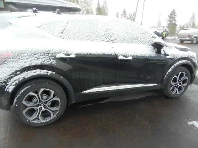 Snöbyar har lagt ett lätt snötäcke på en bil, men har smält på den varma asfalten.