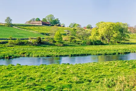 Grönskande jordbrukslandskap. Ett vattendrag rinner bredvid åkrarna.