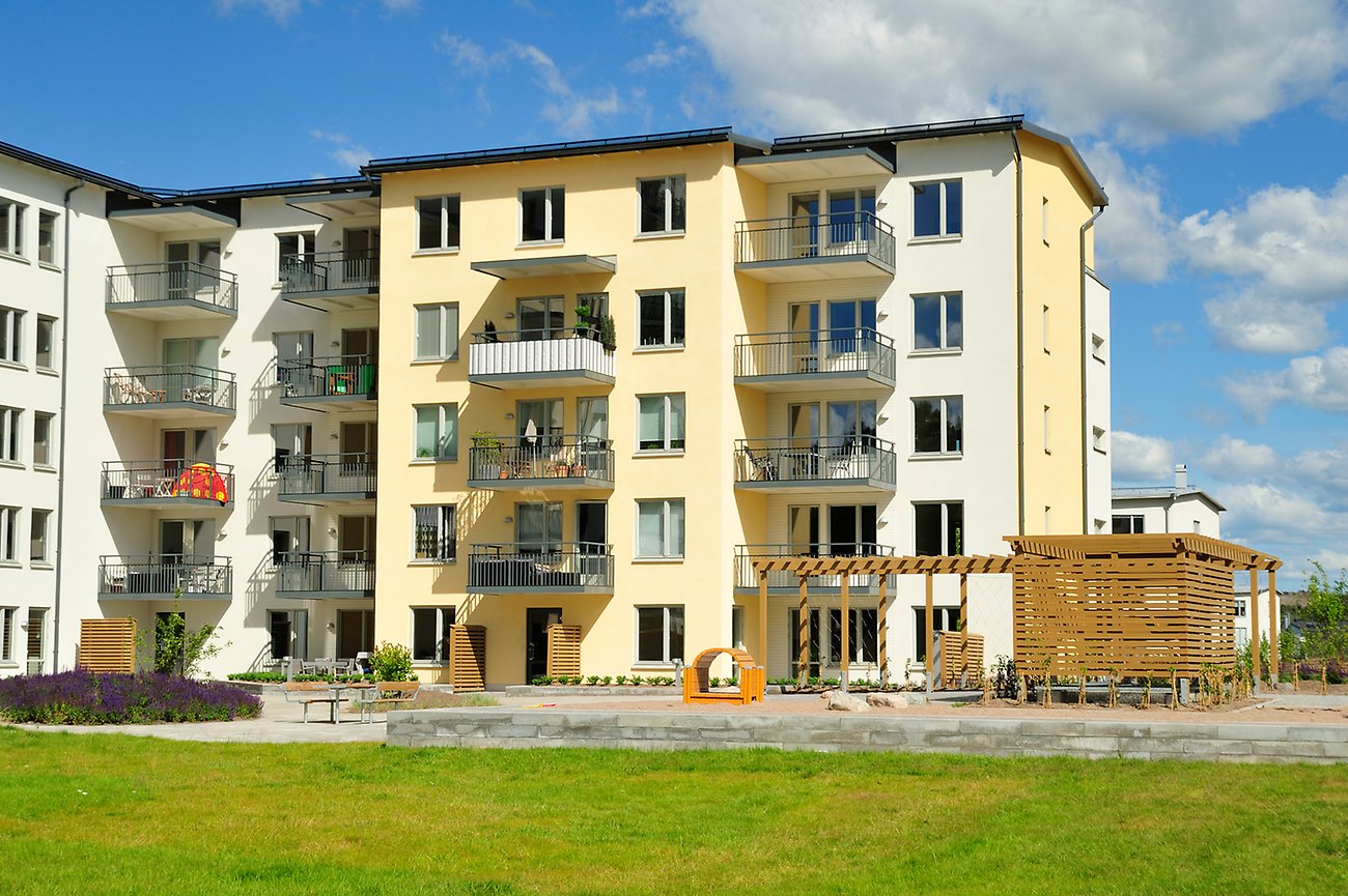 Moderna flerbostadshus i Stockholmsområdet. Grön gräsmatta i förgrunden och blå himmel med moln i bakgrunden.