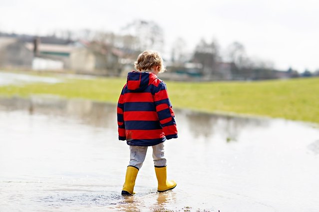 Barn i stövlar går i vatten på översvämmad mark.
