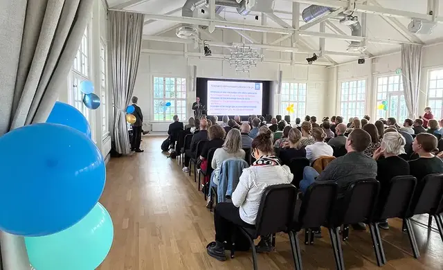 En scen längst fram, publik och blå ballonger i förgrunden.