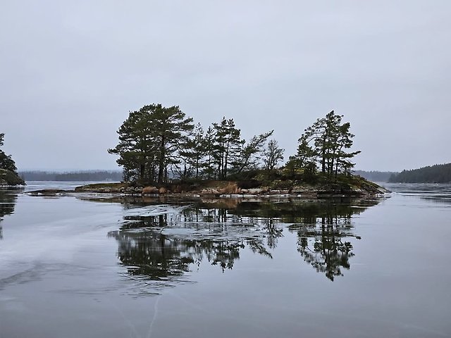 Is på sjö och en holme i sten som sticker upp i horisonten.