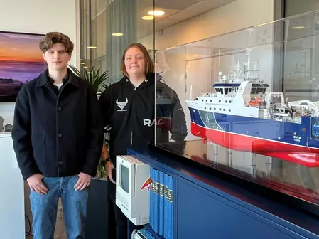 Två killar står bredvid en modell av ett fartyg.