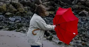 Kvinna håller i ett paraply som viker sig i blåsten och regnet.