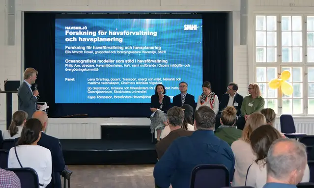 Sittande panel och en moderator på scenen.