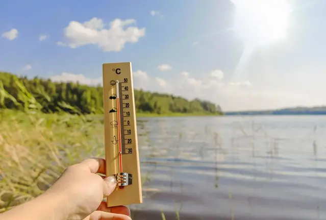 Person håller i en termometer som visar varma temperaturer.