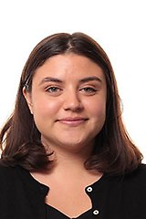 Porträtt av Isadora med axellångt, mörkbrunt hår och svart blus, fotograferad framifrån mot en vit bakgrund.