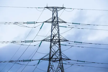 En kraftledningsstolpe sedd snett underifrån mot en himmel med ett molntäcke av varierande tjocka, vita moln i bakgrunden. 