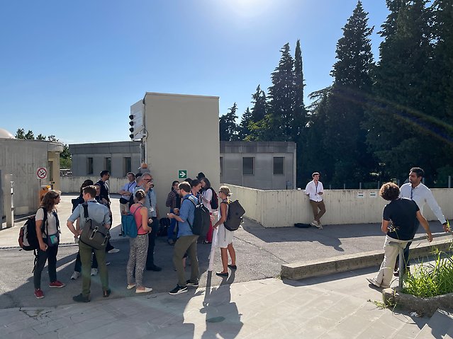 Personer står ute i det soliga vädret och fikar.