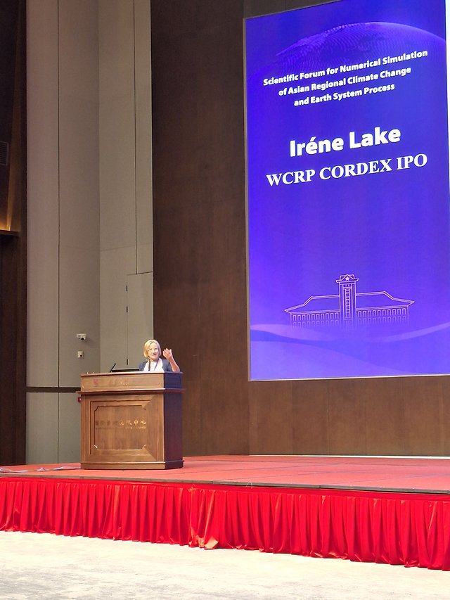 Person standing at a lectern in front of a large screen.