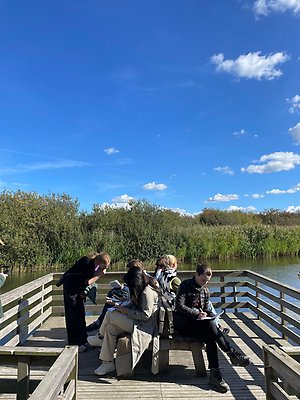 A group of girls sitting on benches, writing, on a small pier.