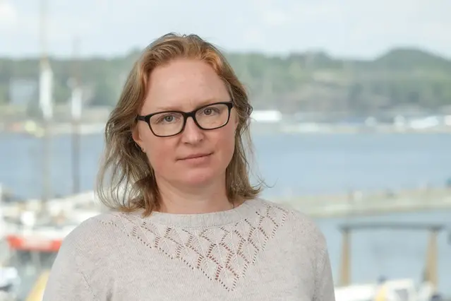 Porträtt på en kvinna, taget inomhus, men med vatten bakom.