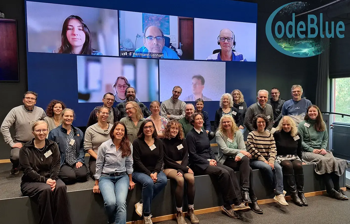 En grupp personer på en scen samt några som är med på bild på en bildskärm bakom dem.