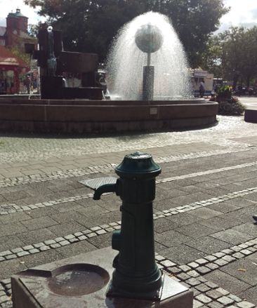 Dricksvattenpost med en fontän i bakgrunden