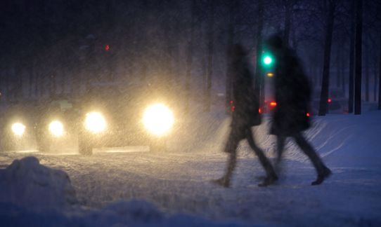 Snöfall i kvällningen med bilar och fotgängare