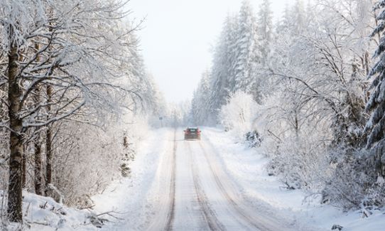 Bil på vintrig skogsväg med snö på träden