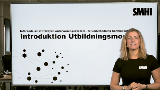 En tjej i svart SMHI t-shirt står framför en presentationsskärm med texten "Introduktion utbildning"