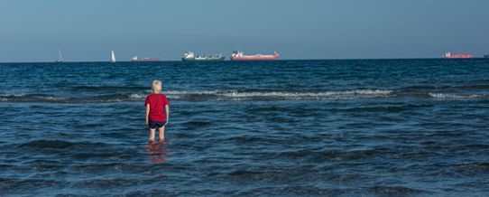 Ett barn badar med fartyg vid horisonten
