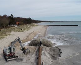 Sand sprutas upp på en strand via ett rör.
