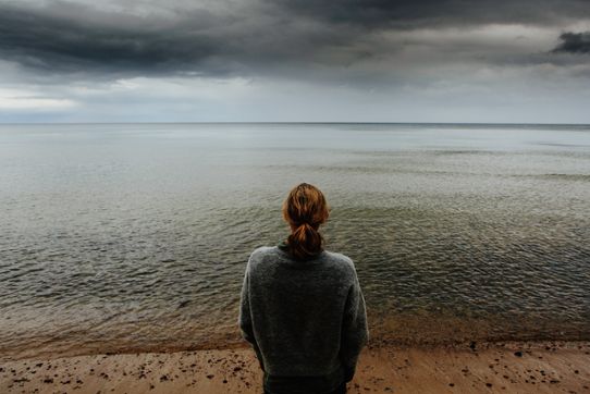 En kvinna blickar ut över havet. Mörka moln.