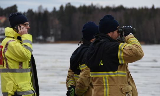 Tre män från räddningstjänsten spanar med kikare och talar i telefon.
