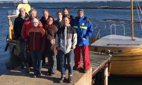 Group photo of nine of the researchers standing in front of a wooden boat