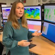 SMHIs meteorolog Marie framför skärmar med kartor och data på meteorologens arbetsplats. 