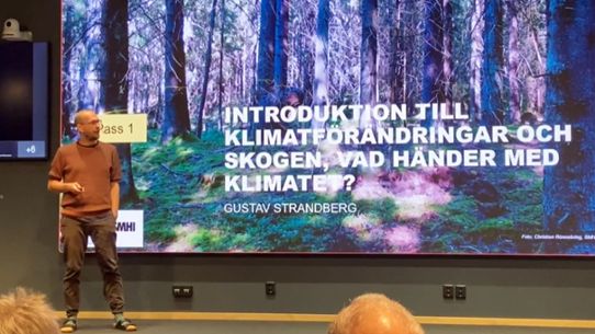 Bild på föreläsare Gustav Strandberg framför en skogsbild.