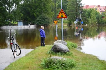 Pojke med cykel tittar på en översvämmad väg.